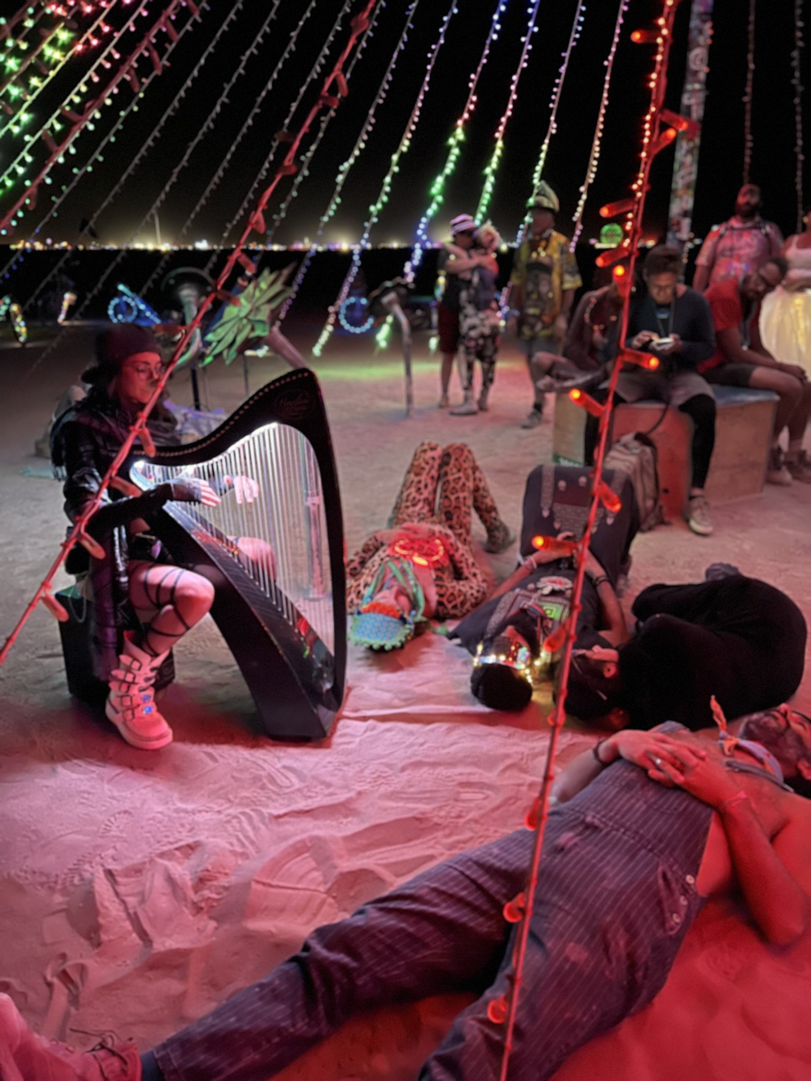 People gathered and reclining around Alycen’s harp at Burning Man