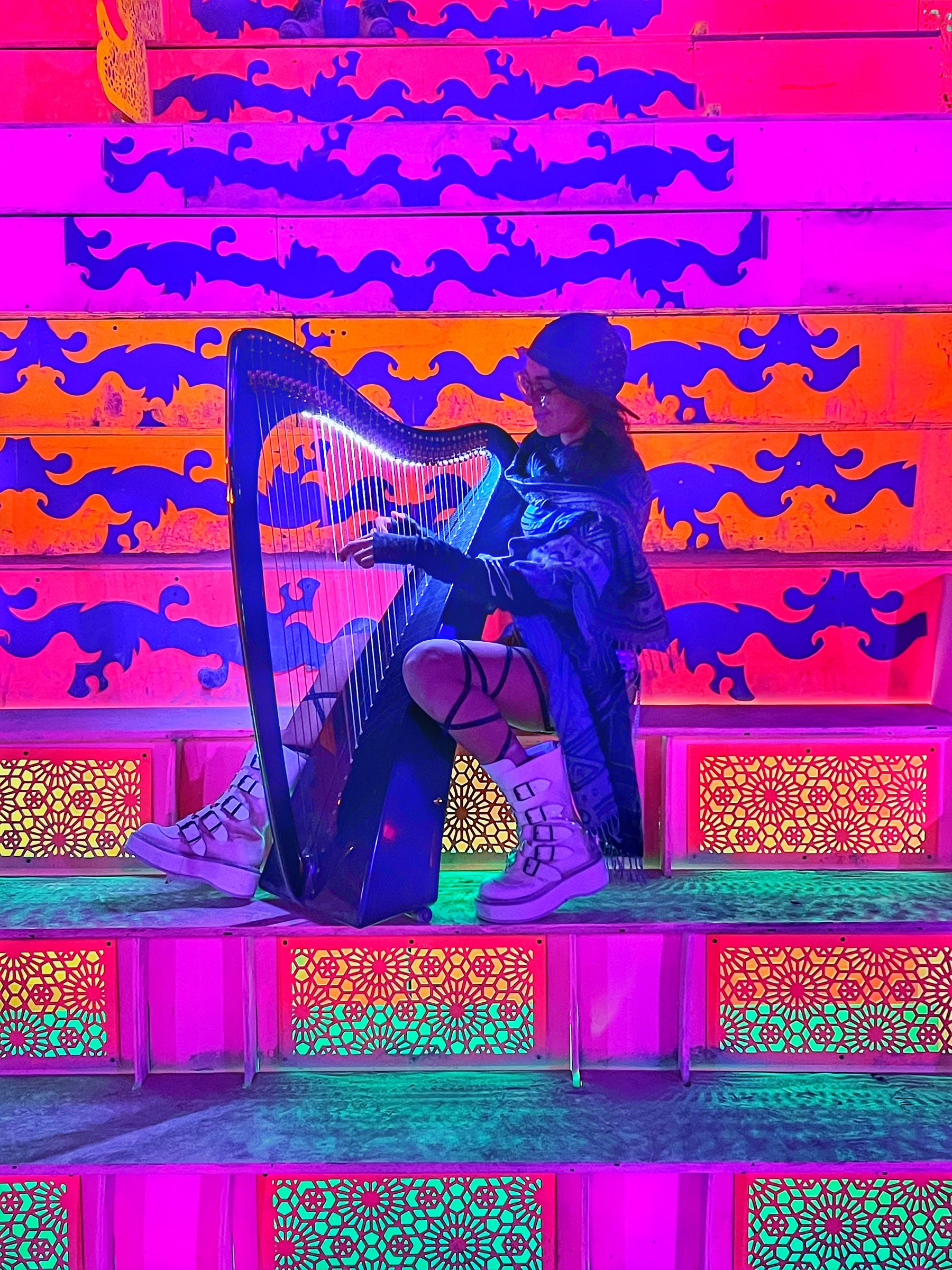 Alycen playing her illuminated harp against colorful psychedelic architecture