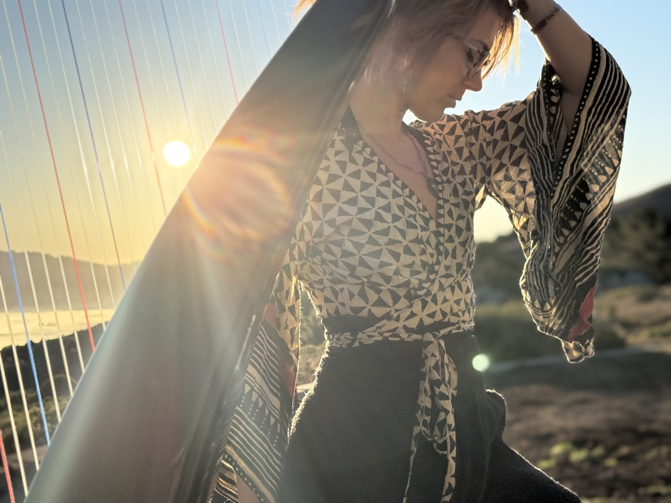 Alycen’s face beside her harp, with golden sunlight passing through the strings on the left